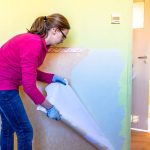 Woman removing old wallpaper from the wall