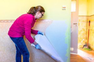 Woman removing old wallpaper from the wall